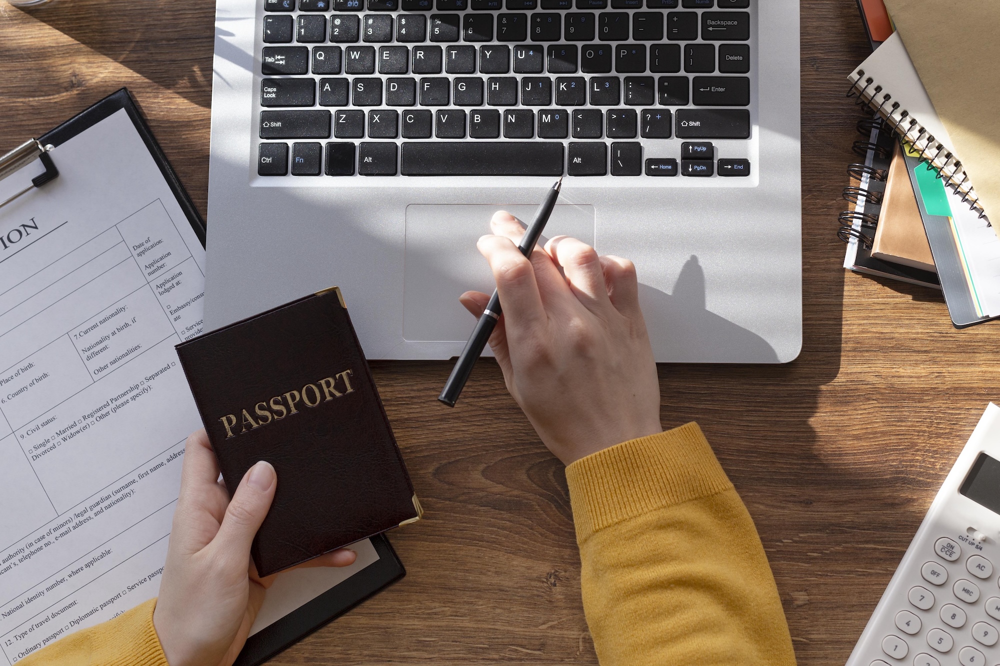Employer reviewing a foreign employee work pass application with a passport, application form, laptop, and calculator.